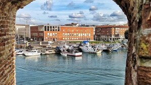 A view through an archway of a marina with boats docked, buildings in the background, and a clear sky. - B&B VillAmorosa (Vicopisano)