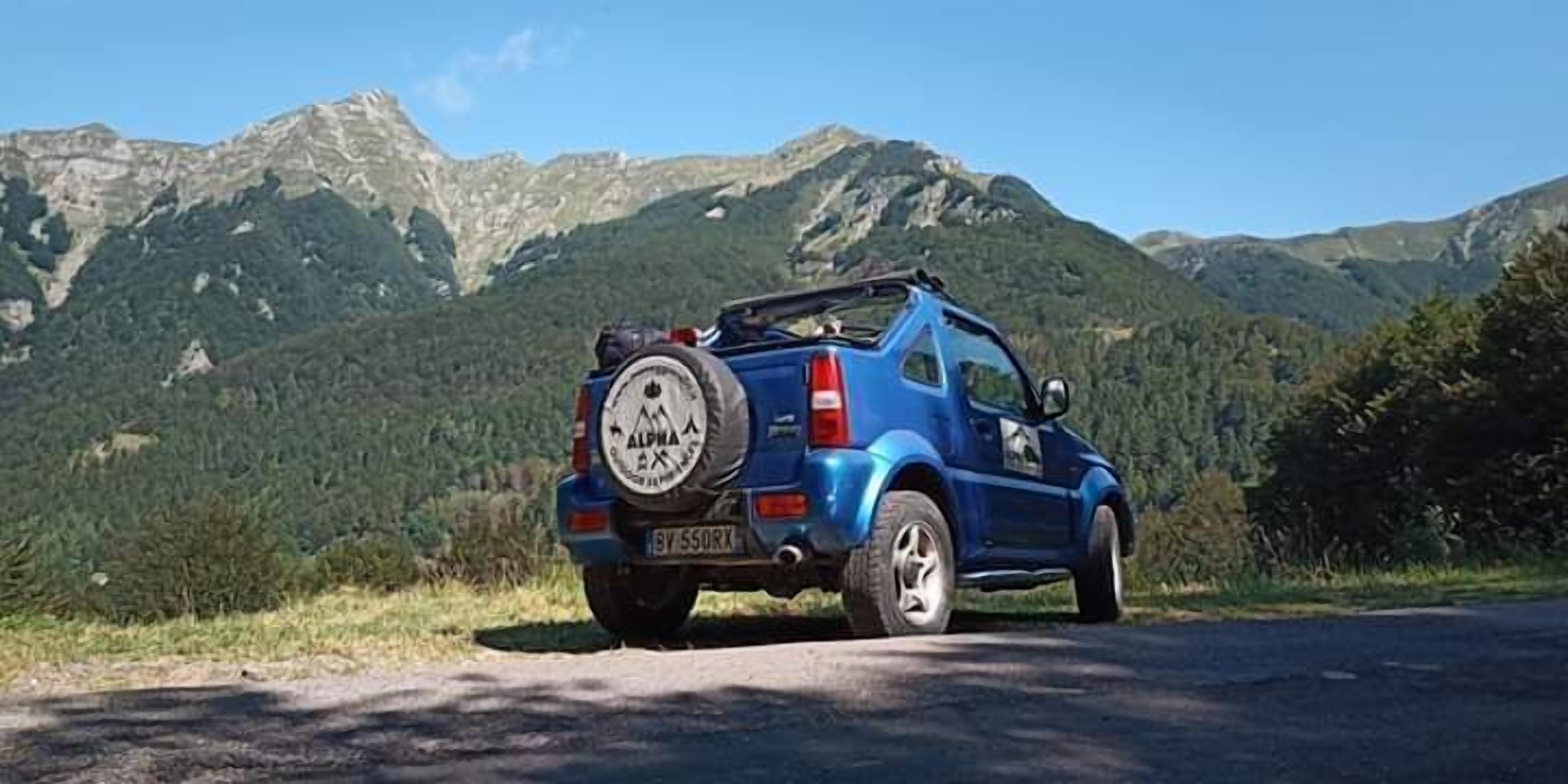 Un SUV bleu est garé sur une route, avec une chaîne de montagnes en arrière-plan.