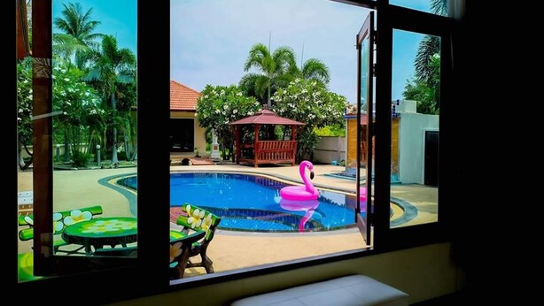 Une piscine avec un flotteur en forme de flamant rose, entourée de palmiers et agrémentée d’un kiosque.