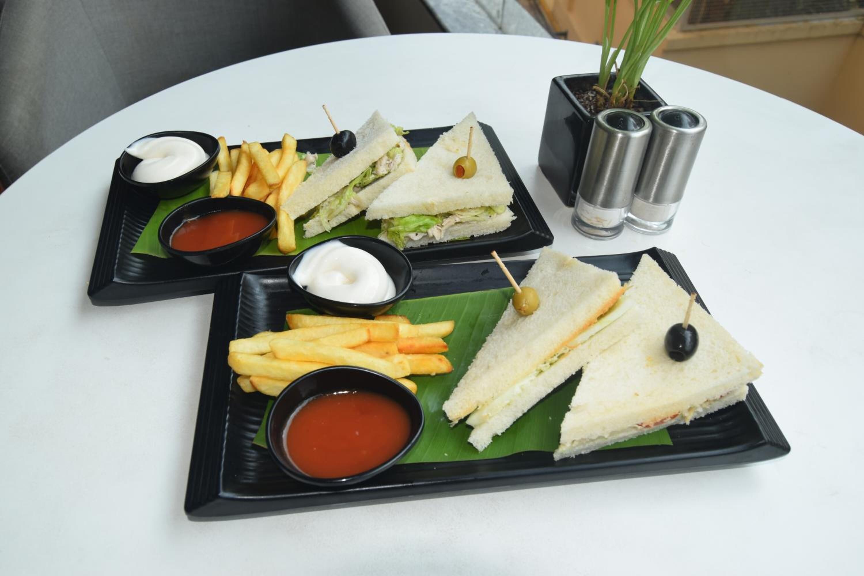 A table with two black trays containing sandwiches, fries, and dipping sauces.