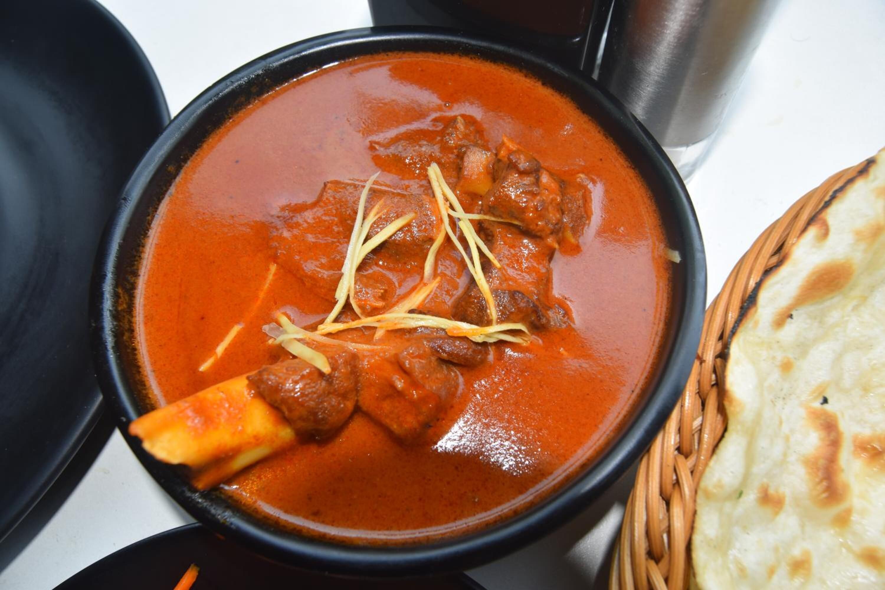 Een kommetje curry met vlees en een stuk naanbrood.