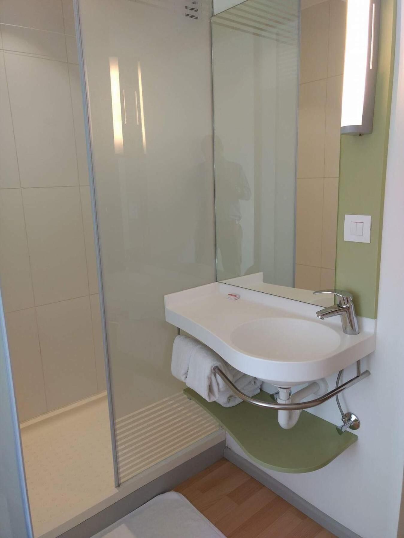 Un baño con cabina de ducha de vidrio, un lavabo blanco con encimera verde y un espejo.