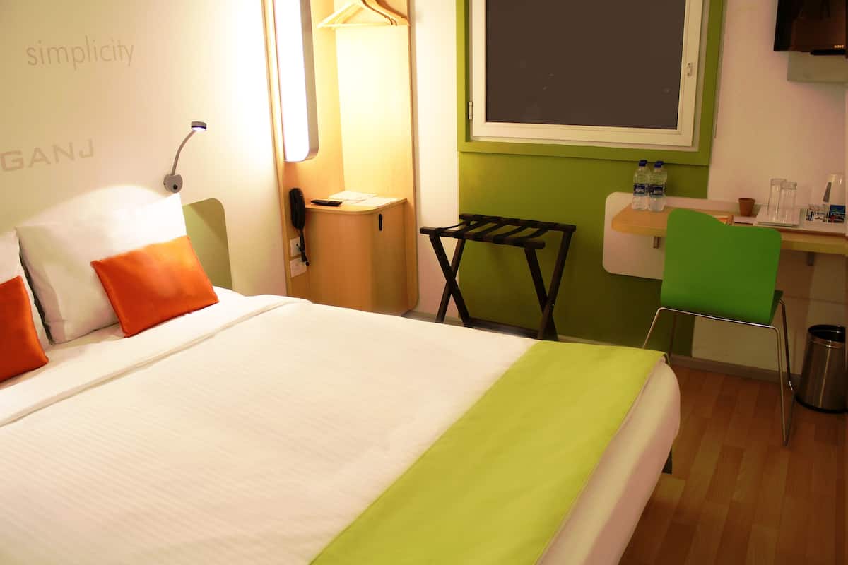 Una habitación de hotel con una cama, un escritorio, una silla y una mesita con botellas de agua.