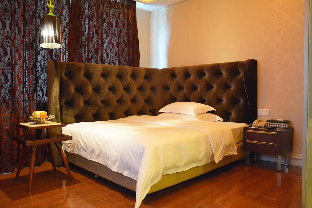 A bedroom with a tufted headboard, a bedside table with a lamp, a bedside telephone, and a small table with a candle and flowers.