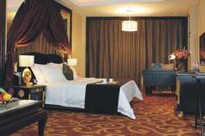 Ein Hotelzimmer mit einem großen Bett, einem Schreibtisch mit Laptop, einer Schreibtischlampe und einer Vase mit Blumen.