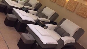Ein Zimmer mit in Reih und Glied angeordneten Massagesesseln, einem großen Fenster mit Vorhängen und Wandleuchten.