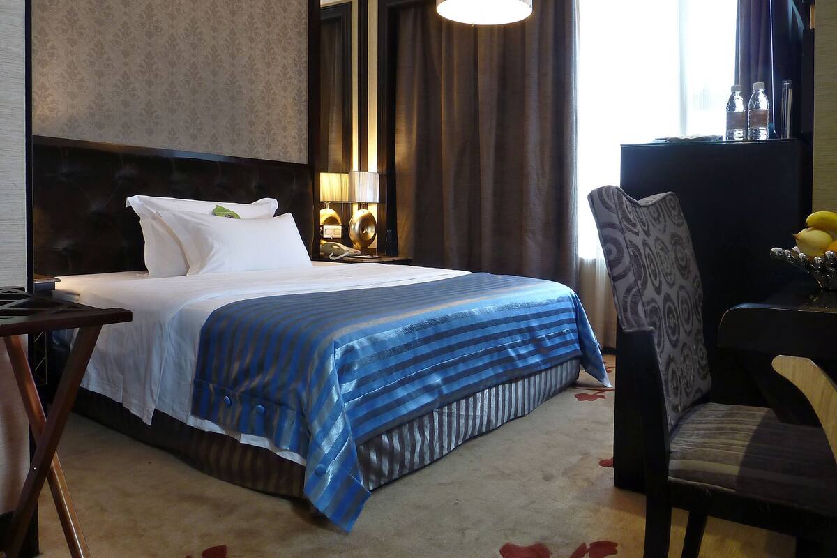 A hotel room with a large bed, a desk, a chair, and a lamp.