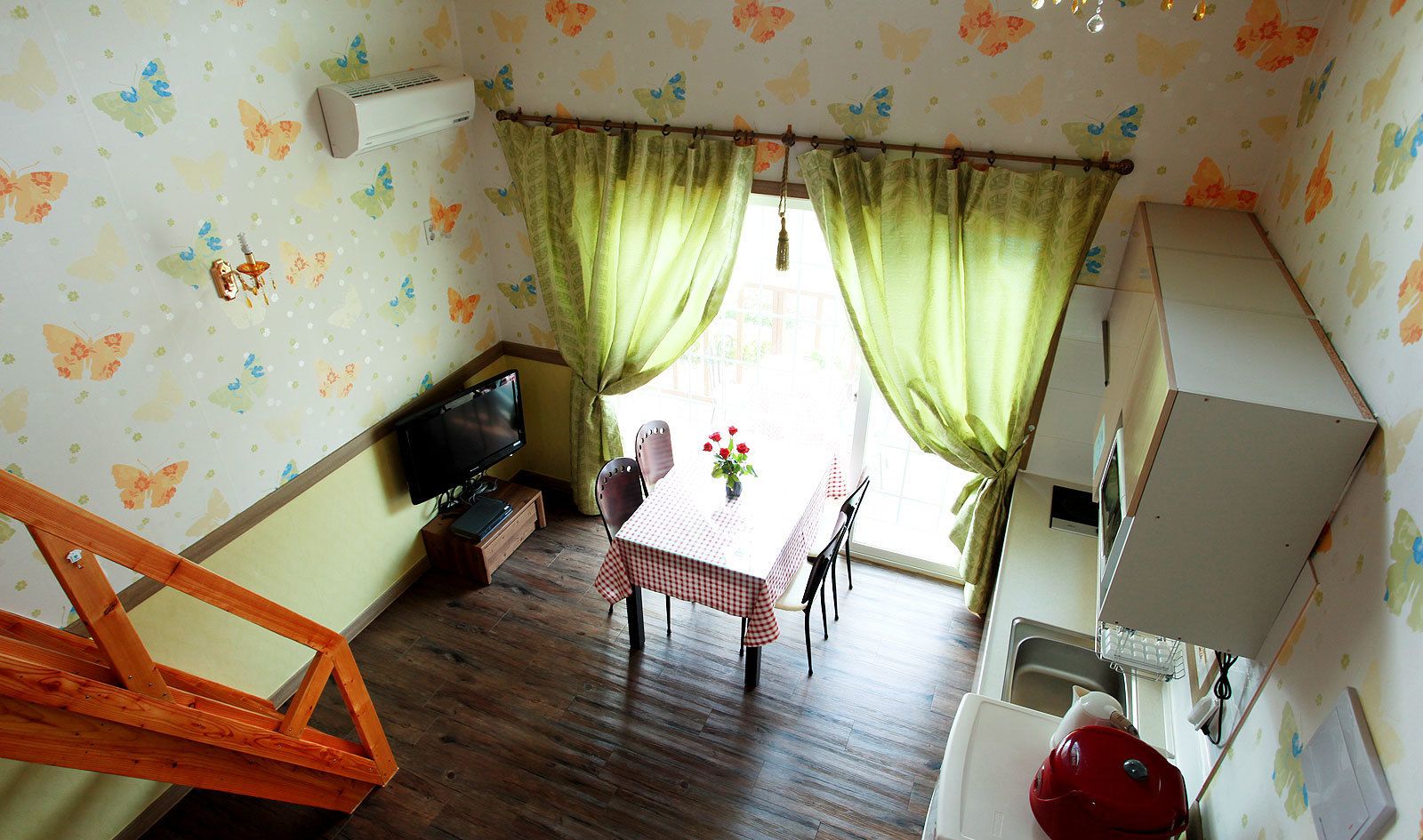A compact room with a dining table, chairs, a television, and a kitchenette.