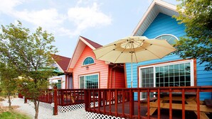 Ein farbenfrohes Haus mit roter und blauer Fassade, einer Holzterrasse und einem großen Sonnenschirm.
