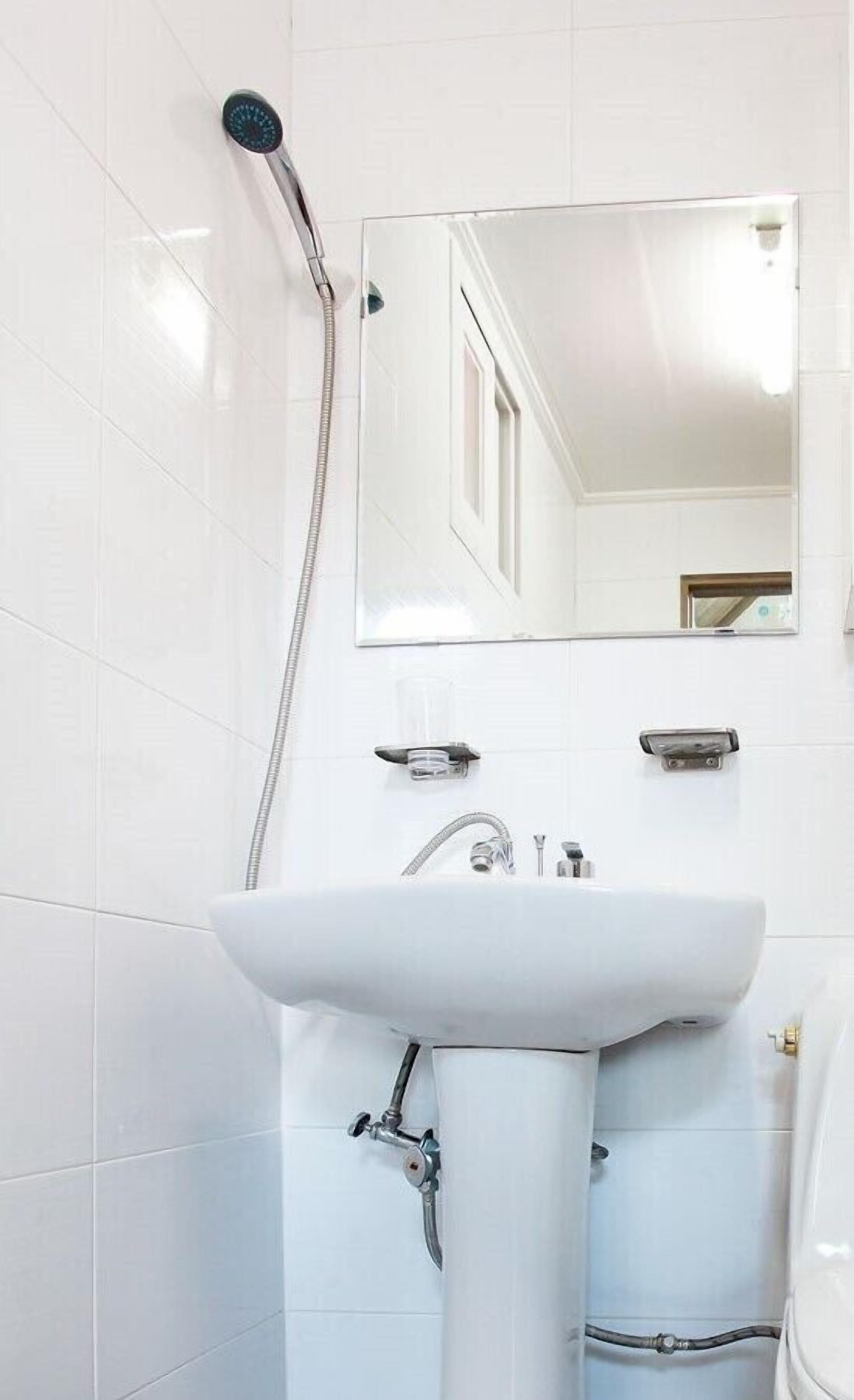 Une salle de bain avec des carreaux blancs, un lavabo, un miroir et une pomme de douche.
