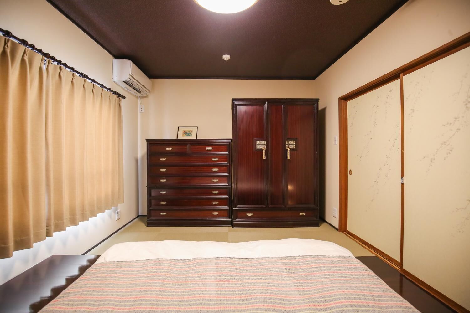 A bedroom with a bed, a wardrobe, a window with curtains, and a ceiling light.