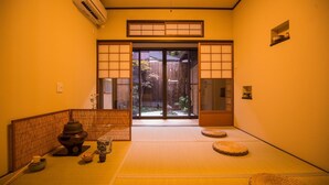 Um quarto japonês tradicional com tatames, uma porta de tela shoji e uma pequena área de assento com tatames.