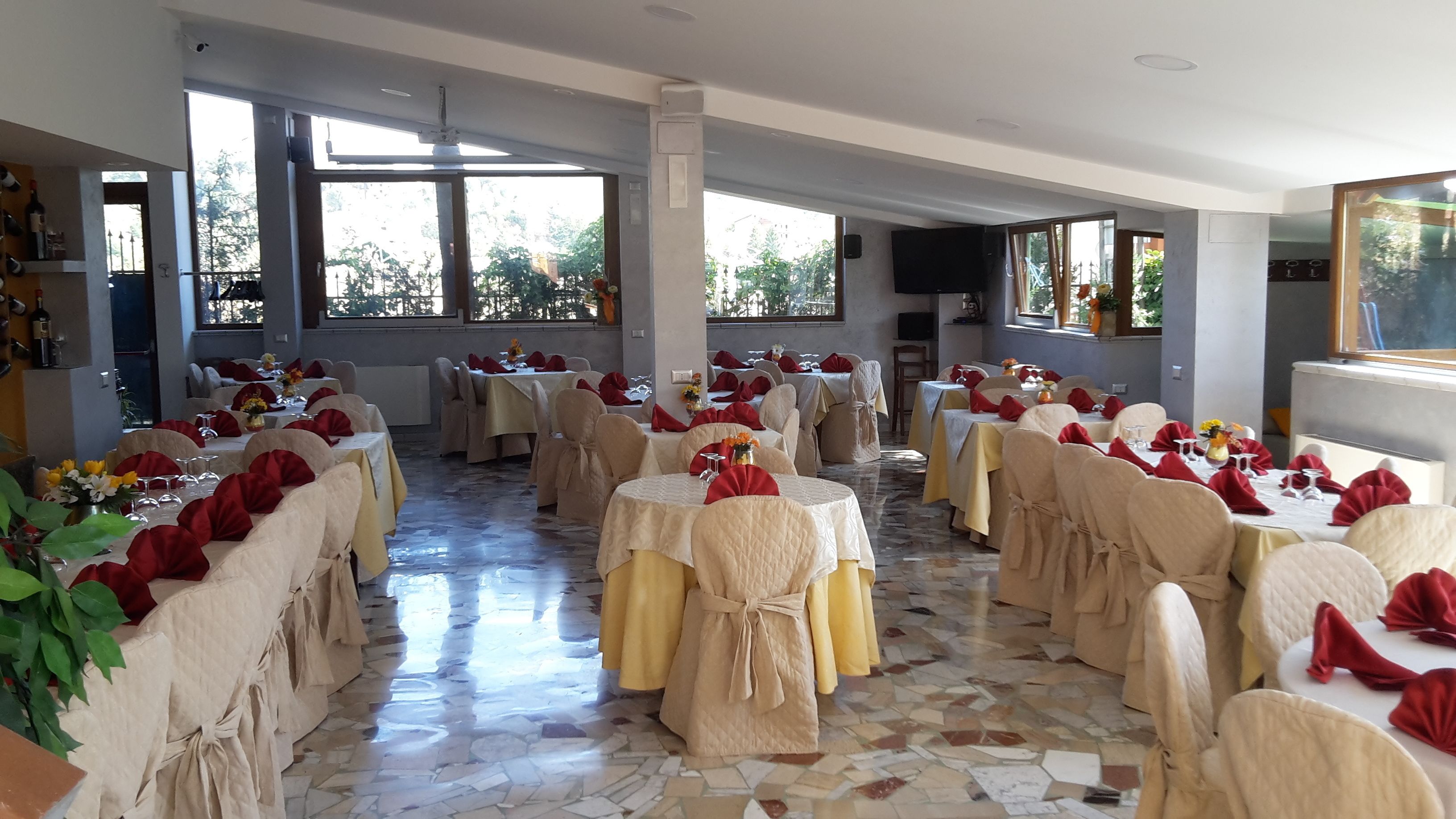 Una sala da banchetti con tavoli rotondi, sedie beige e tovaglioli rossi.