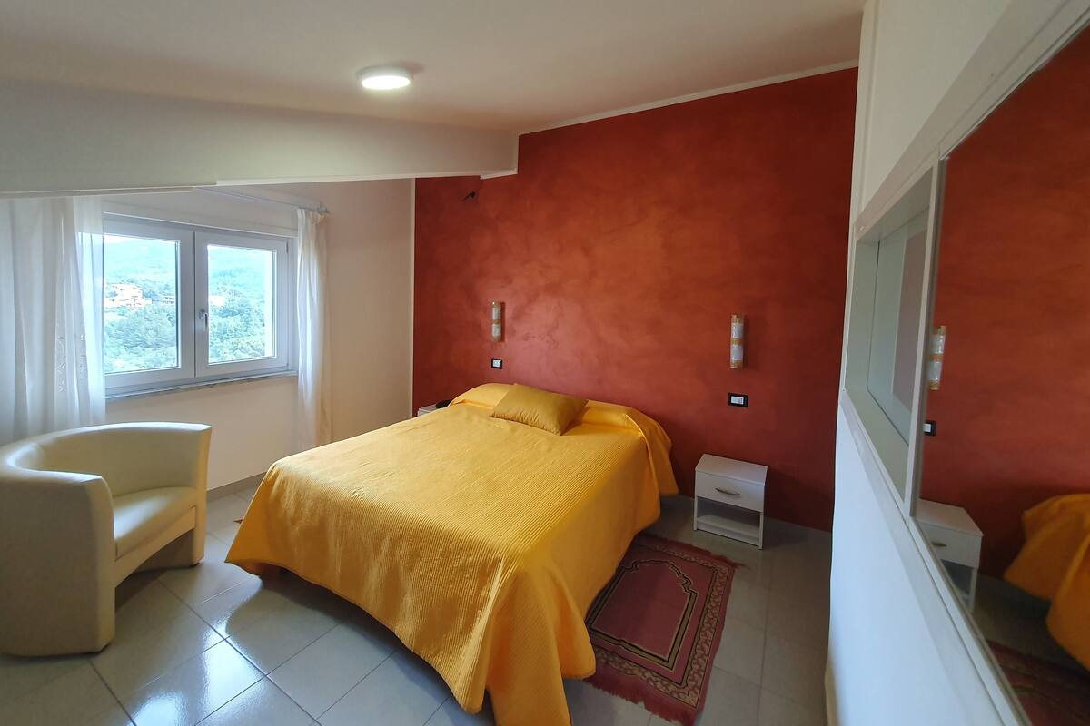 A bedroom with a bed, a chair, a nightstand, and a window with curtains.