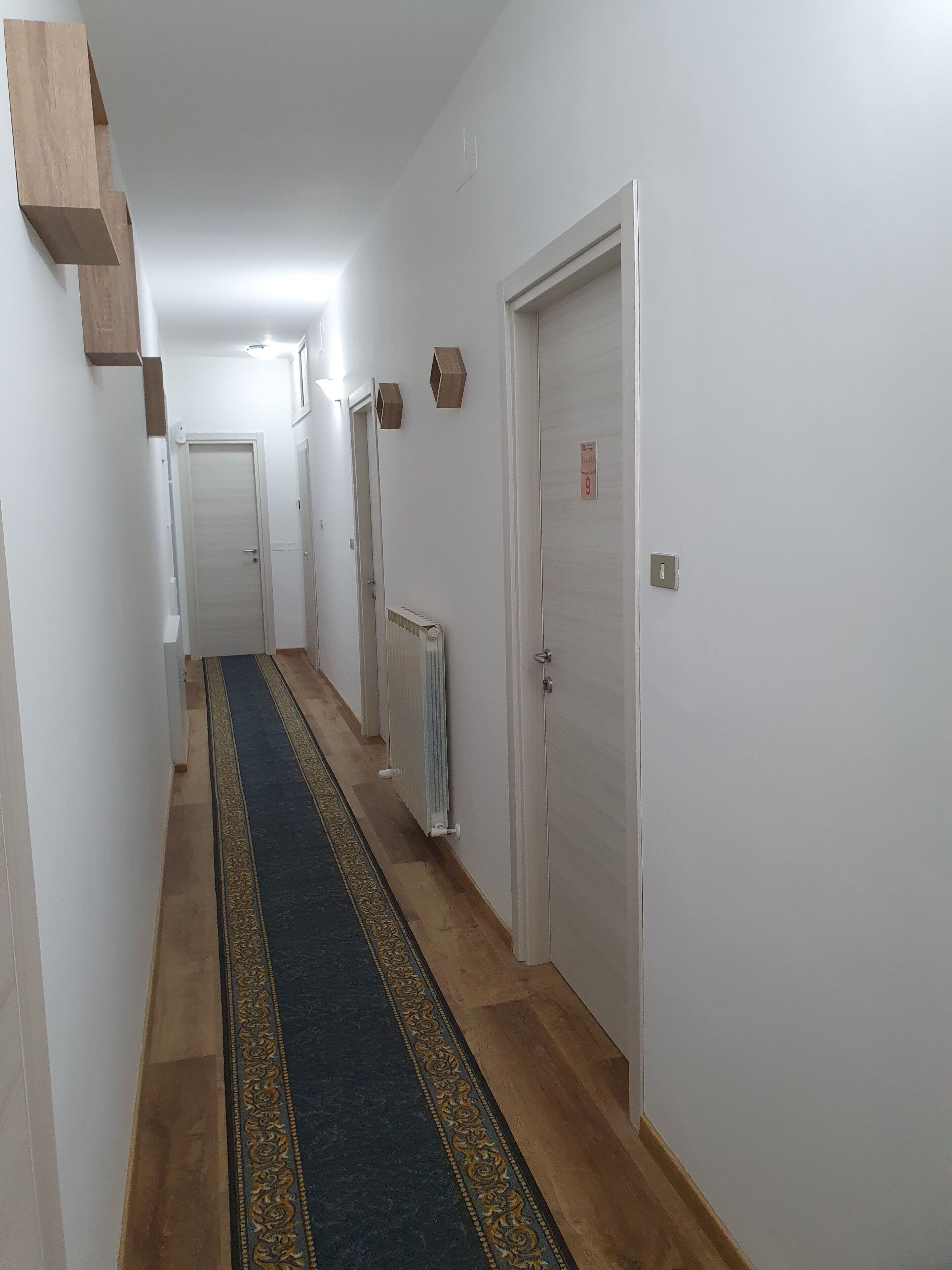 A narrow hallway with a patterned carpet, white walls, and a radiator.