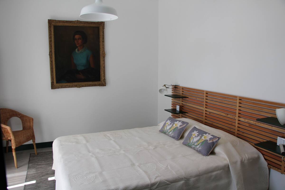 A neatly arranged bedroom with a bed, a chair, a bedside table, and a wall-mounted lamp.