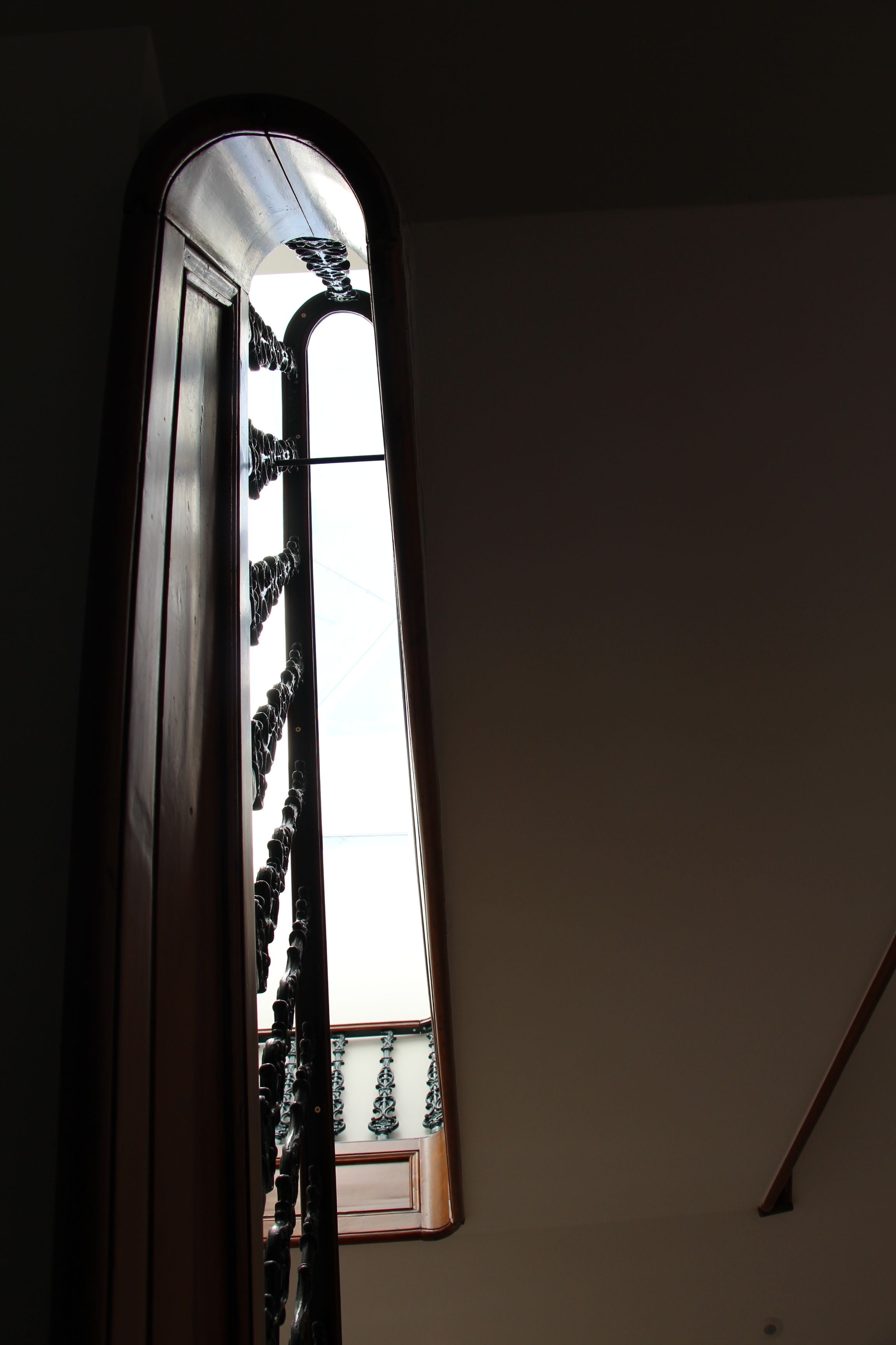 Vista a través de una ventana con marco de madera y barandilla metálica, mostrando un breve vistazo a un balcón con barandas decorativas.