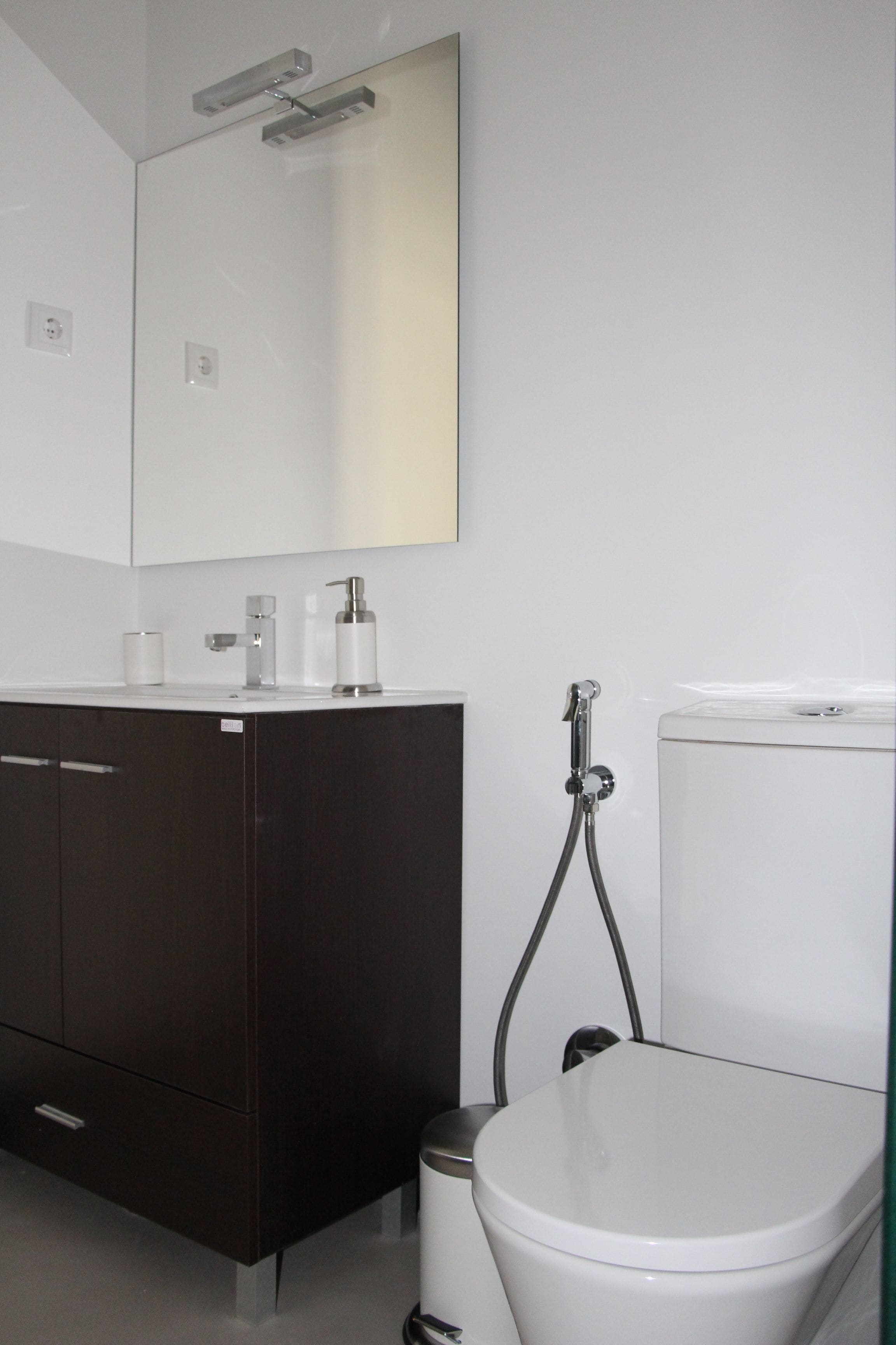 Een moderne badkamer met een donker houten wastafelmeubel, een wit toilet en een spiegel bevestigd aan de muur.