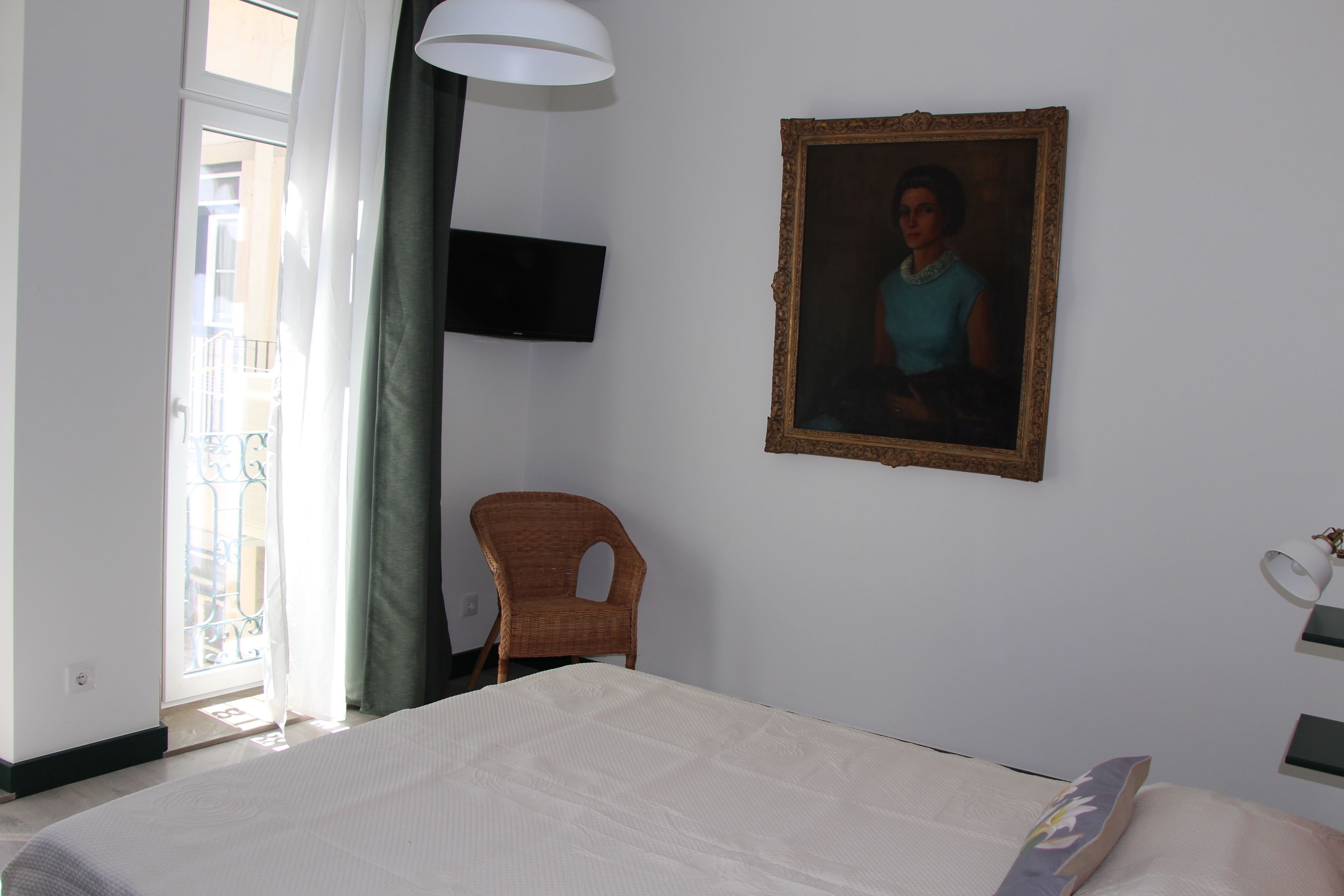 Un dormitorio con cama, una silla, televisor montado en la pared y un cuadro.