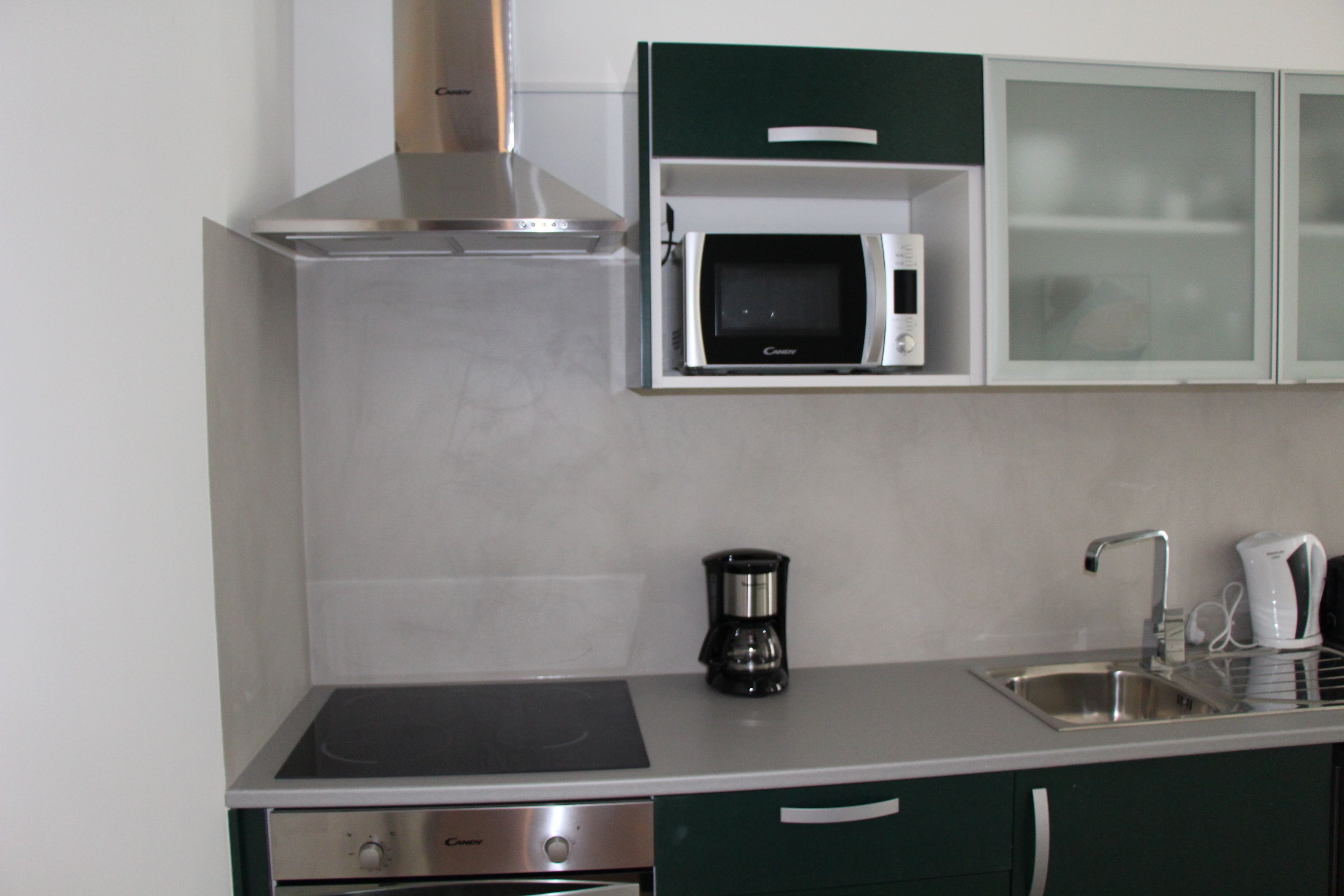 Una cocina moderna con microondas integrado, cafetera y campana extractora de acero inoxidable.