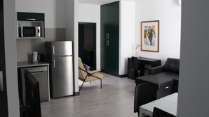 A modern kitchen with a microwave, refrigerator, and dishwasher. There is a beige chair and a black sofa in the living area. - DoBairro Suites at Bairro Alto (Lisbon)
