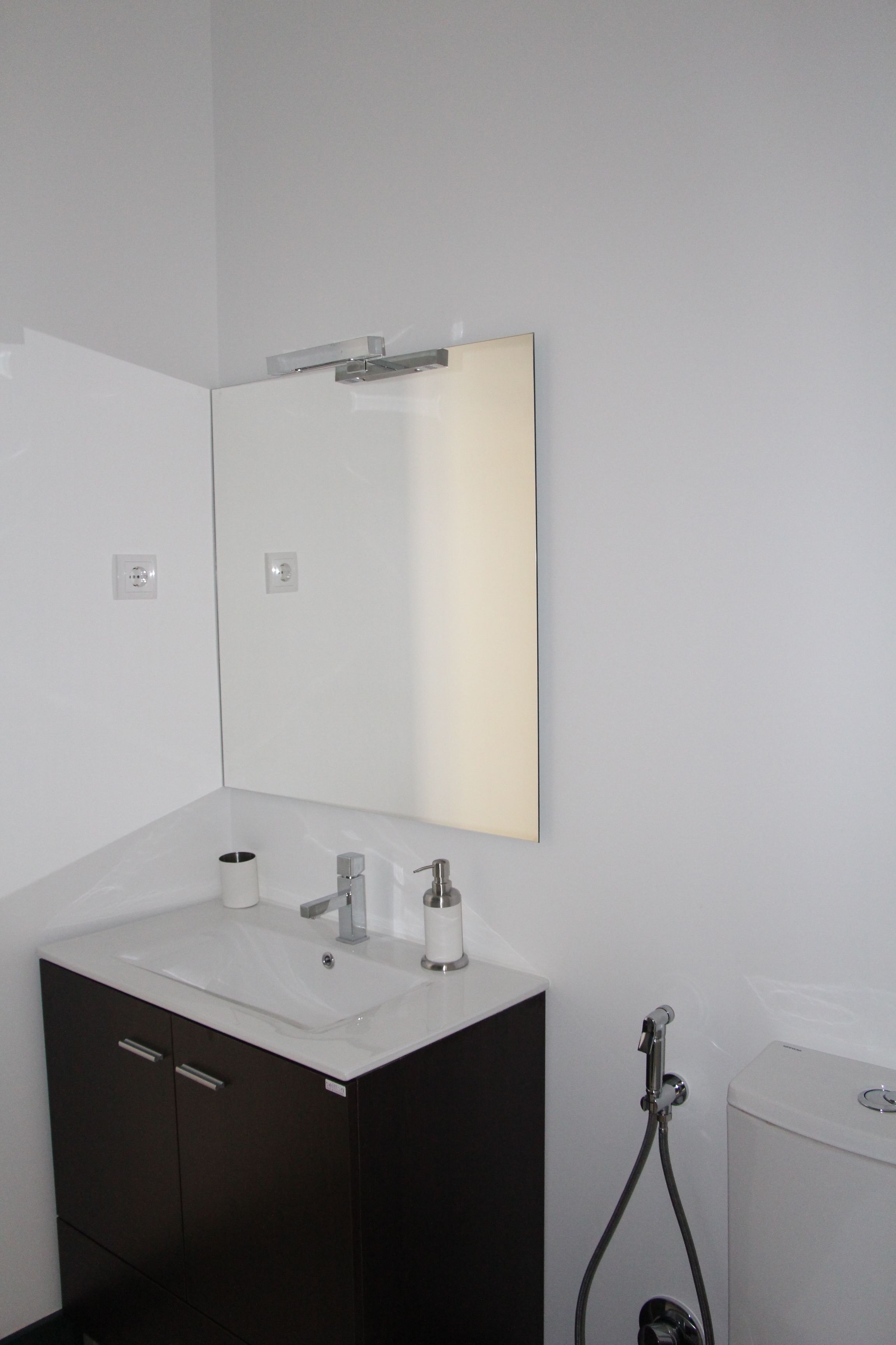 A modern bathroom with a white sink, dark cabinet, and a mirror.