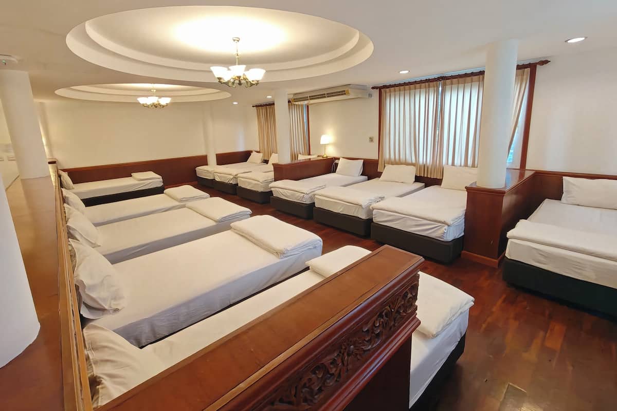 A hotel room with six neatly made beds arranged in two rows, a chandelier, and a large window with curtains.