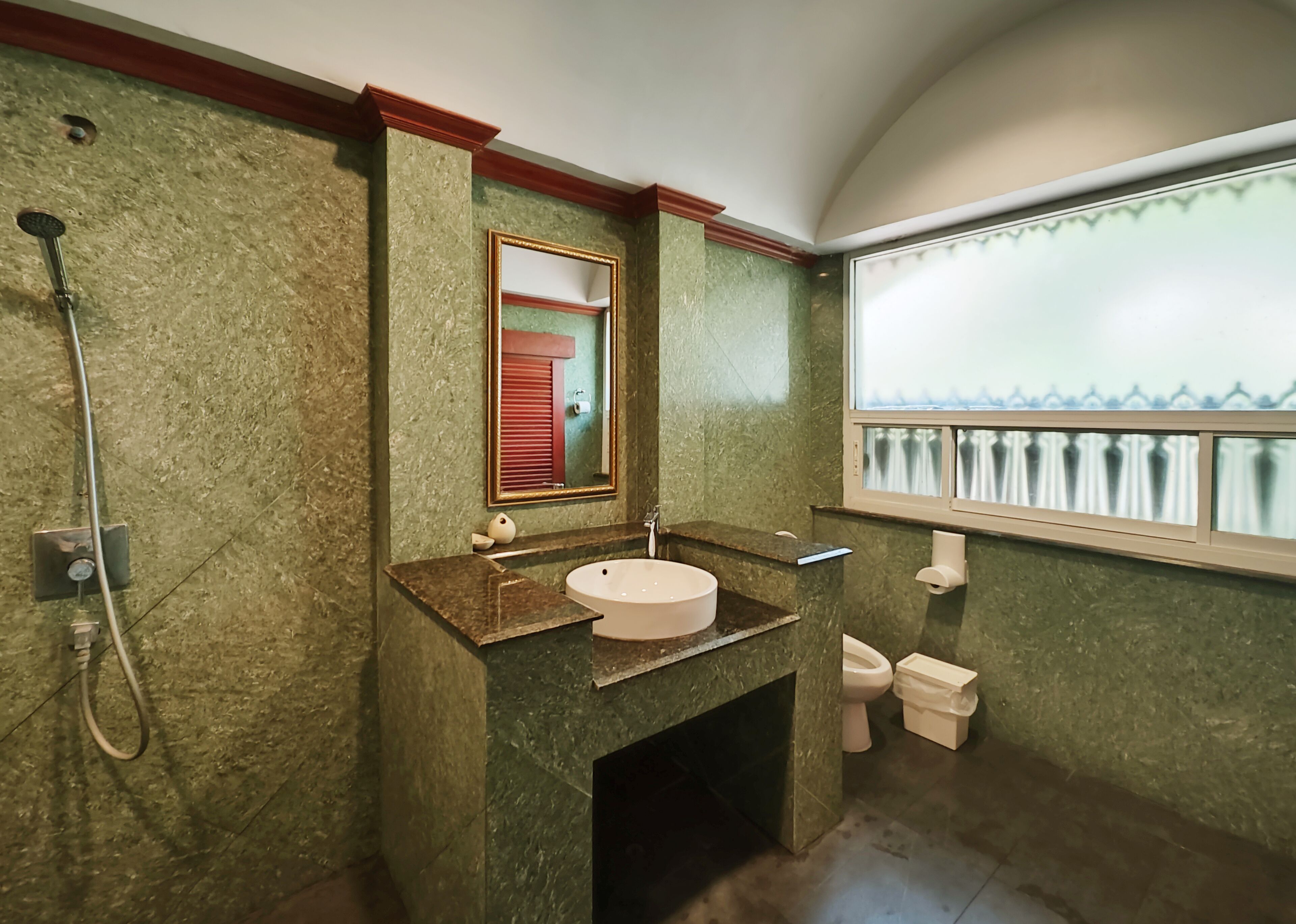 A bathroom with a marble wall, a sink with a mirror, a shower, and a toilet.