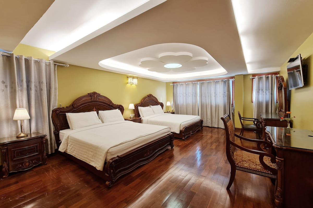 A hotel room with two beds, wooden furniture, a chandelier, and a TV.