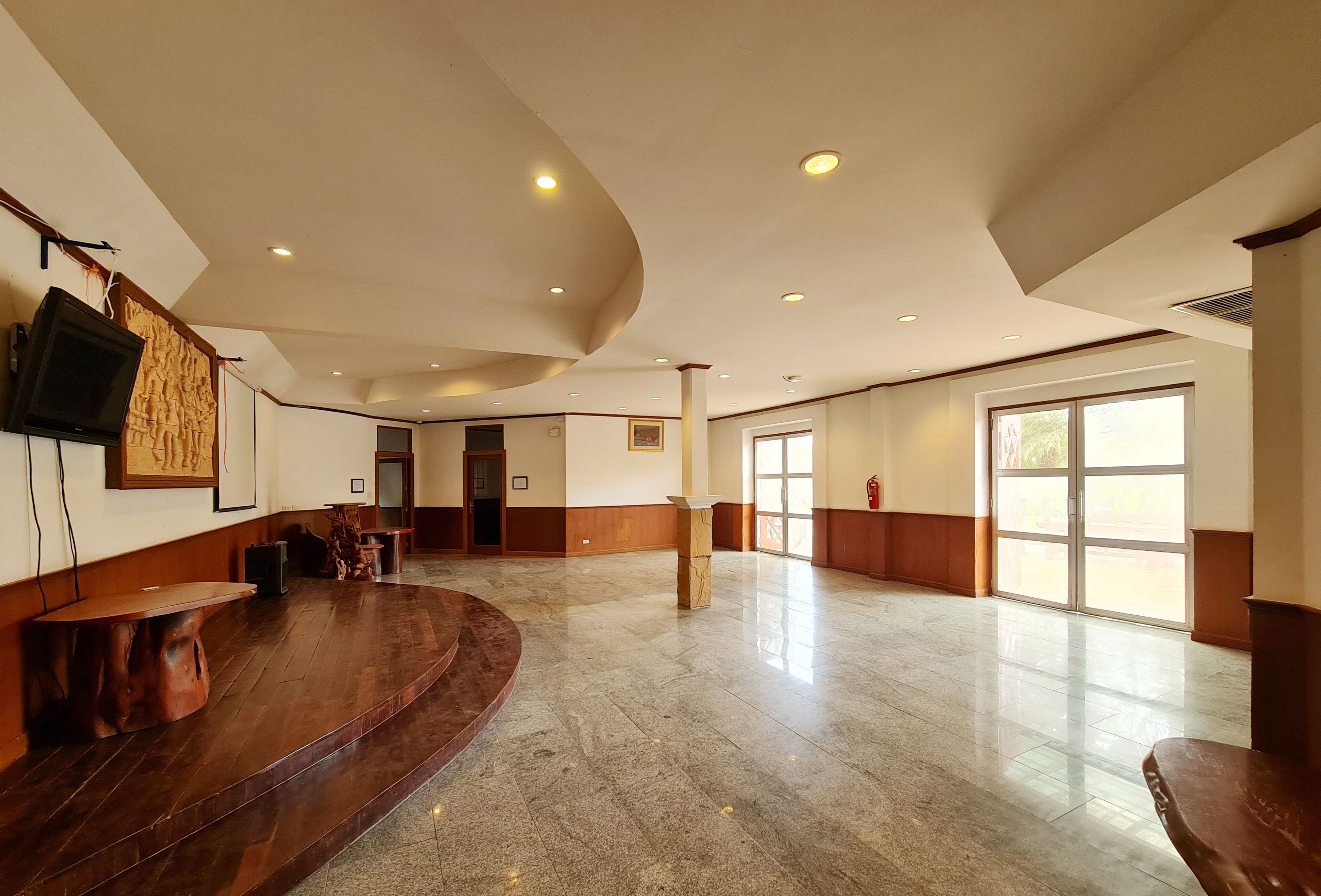 Un hall amplio con un mostrador de recepción curvo de madera, un televisor de pantalla plana en la pared y un gran ventanal que proporciona luz natural.