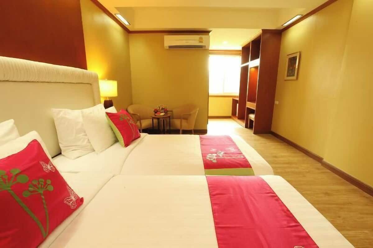 A hotel room with a bed, a small table with chairs, an air conditioning unit, and a window.