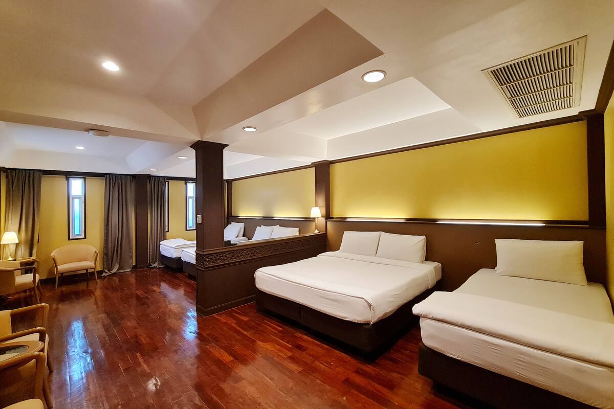 A hotel room with a large bed, two smaller beds, a desk, and a chair.