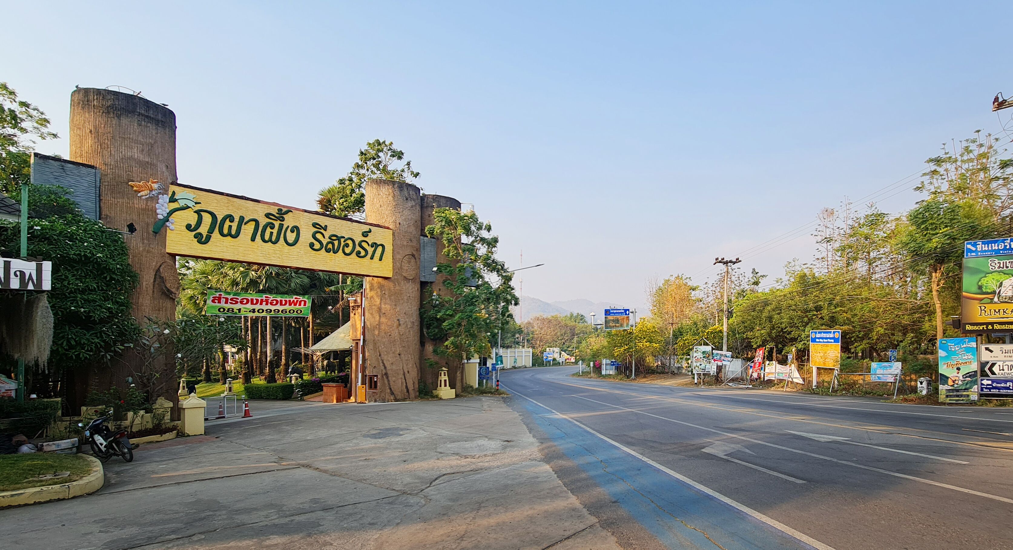 Une vue de rue avec une grande enseigne pour un hôtel appelé  « Nangio Saosn » et une plus petite enseigne pour « Khao Suan », avec un numéro de téléphone.