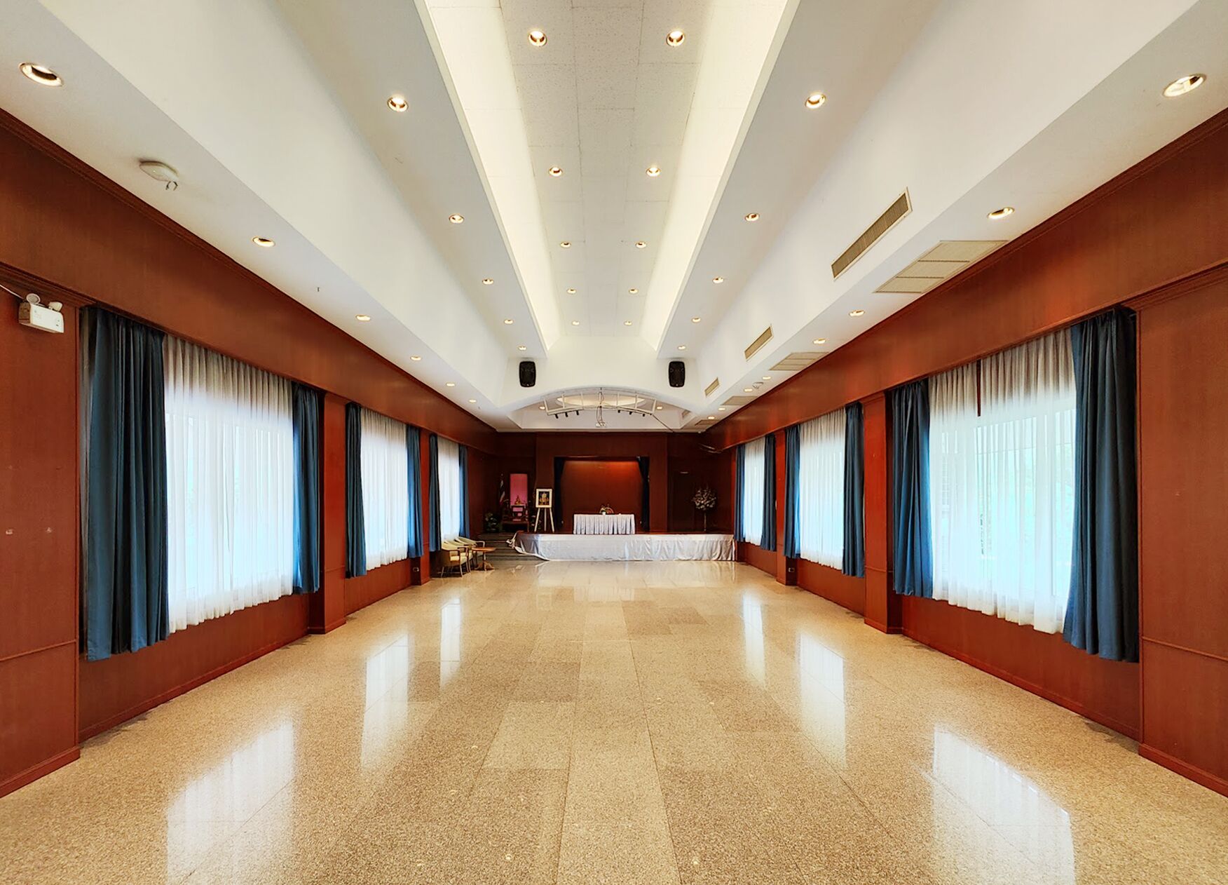 A spacious hotel lobby with a high ceiling, polished floors, and large windows with blue curtains.