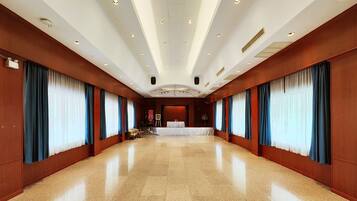 A spacious hotel lobby with a high ceiling, polished floors, and large windows with blue curtains.