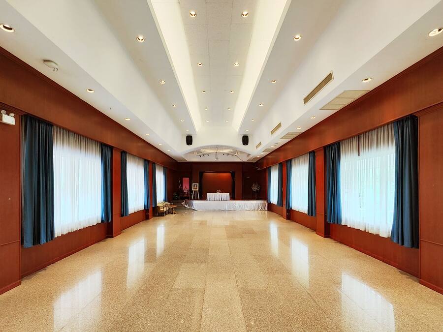 A spacious hotel lobby with a high ceiling, polished floors, and large windows with blue curtains.