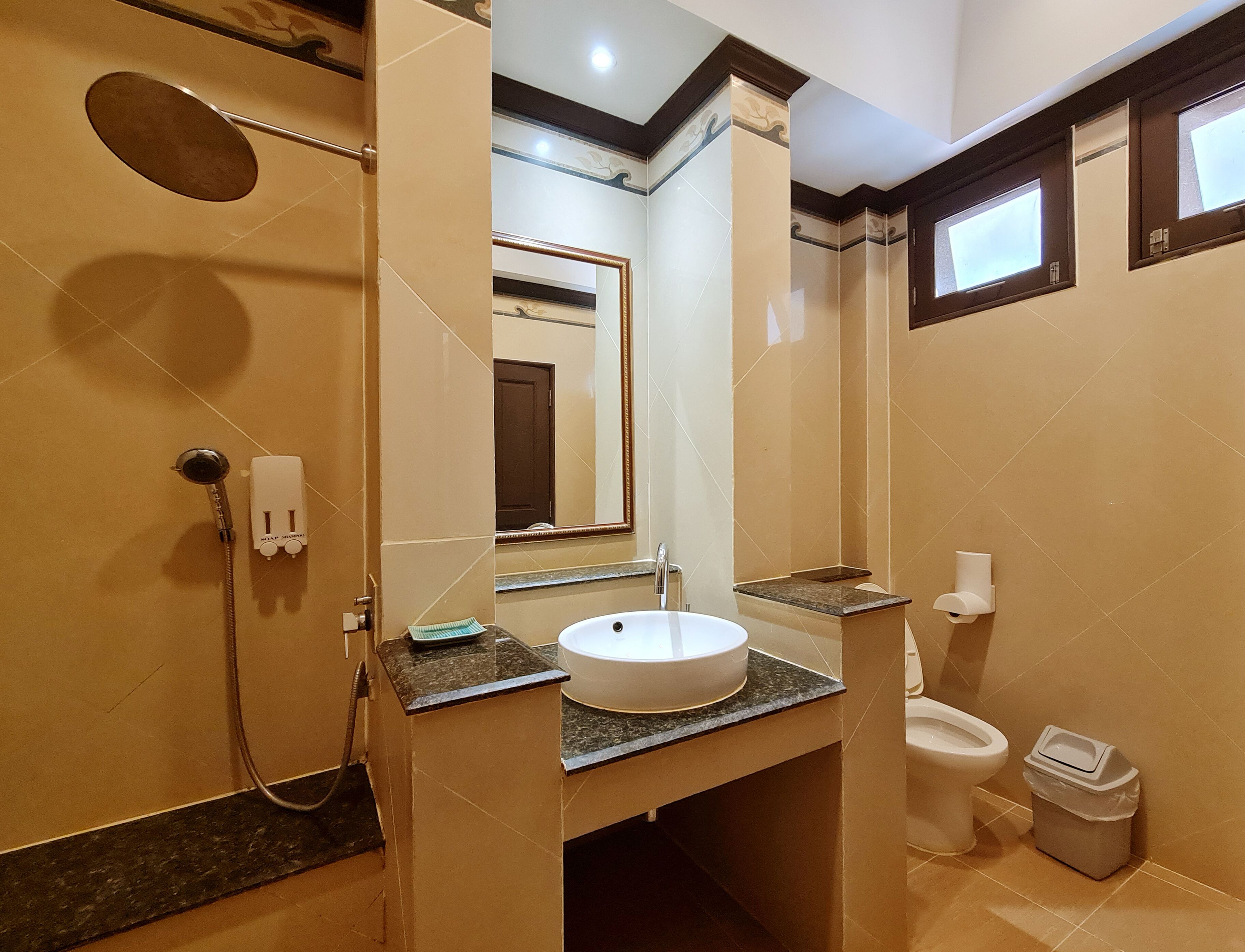 A bathroom with a shower, sink, toilet, and a trash bin.