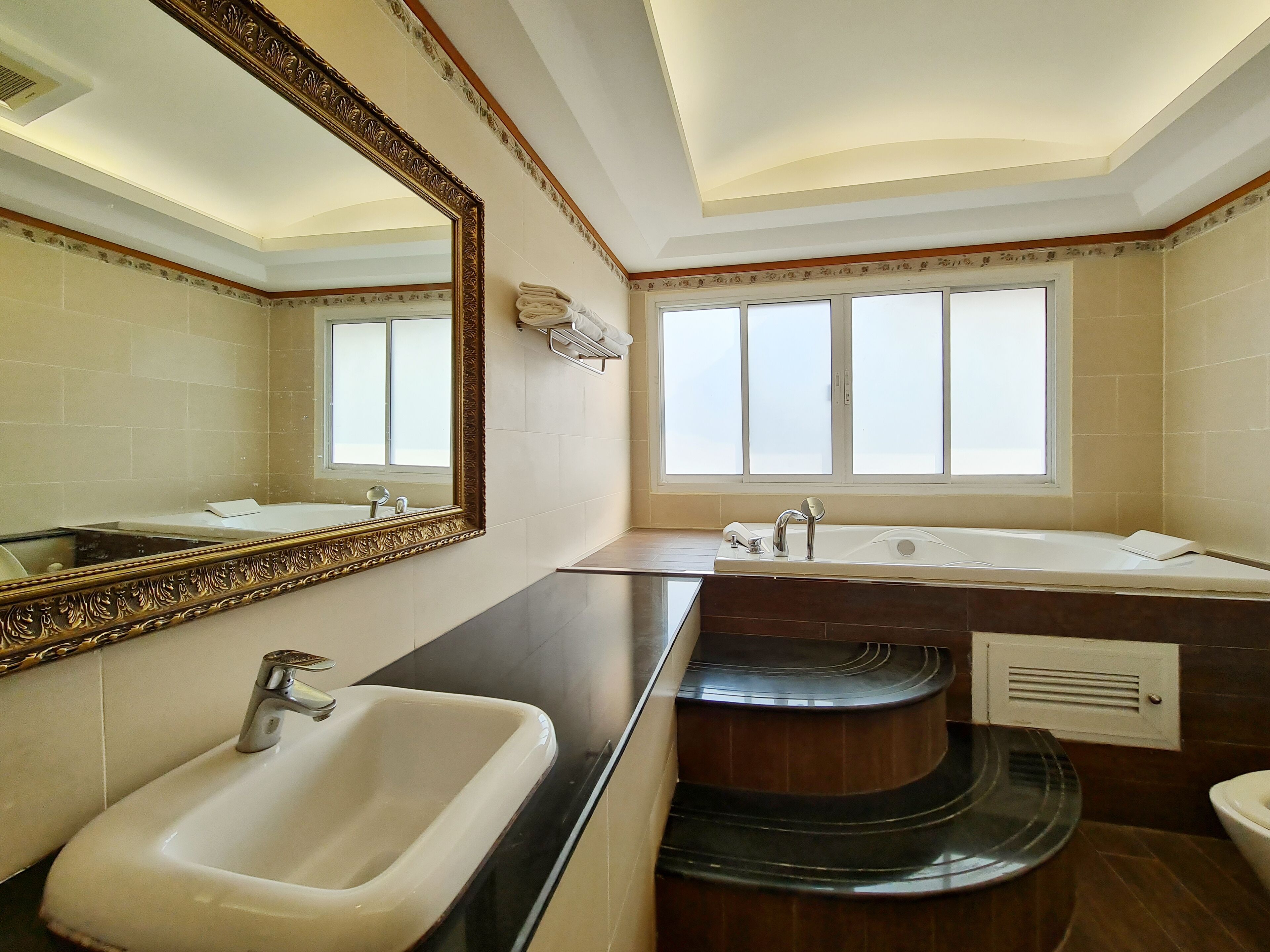 A bathroom with a large mirror, a sink, a bathtub, and a window.