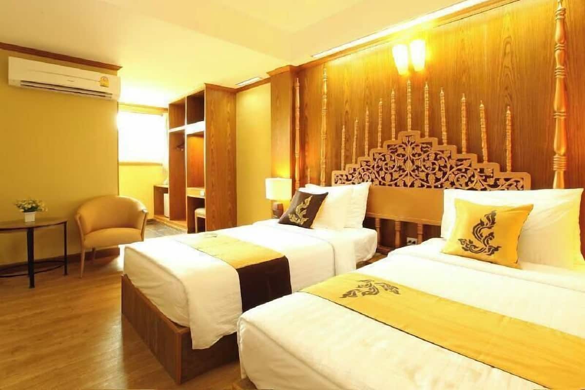 A hotel room with two beds, a wooden headboard, a small table with a chair, and a wardrobe.