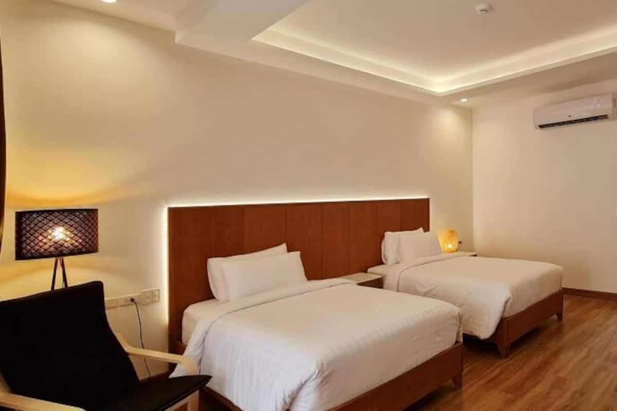 A hotel room with two beds, a desk, a chair, a TV, and a desk lamp.