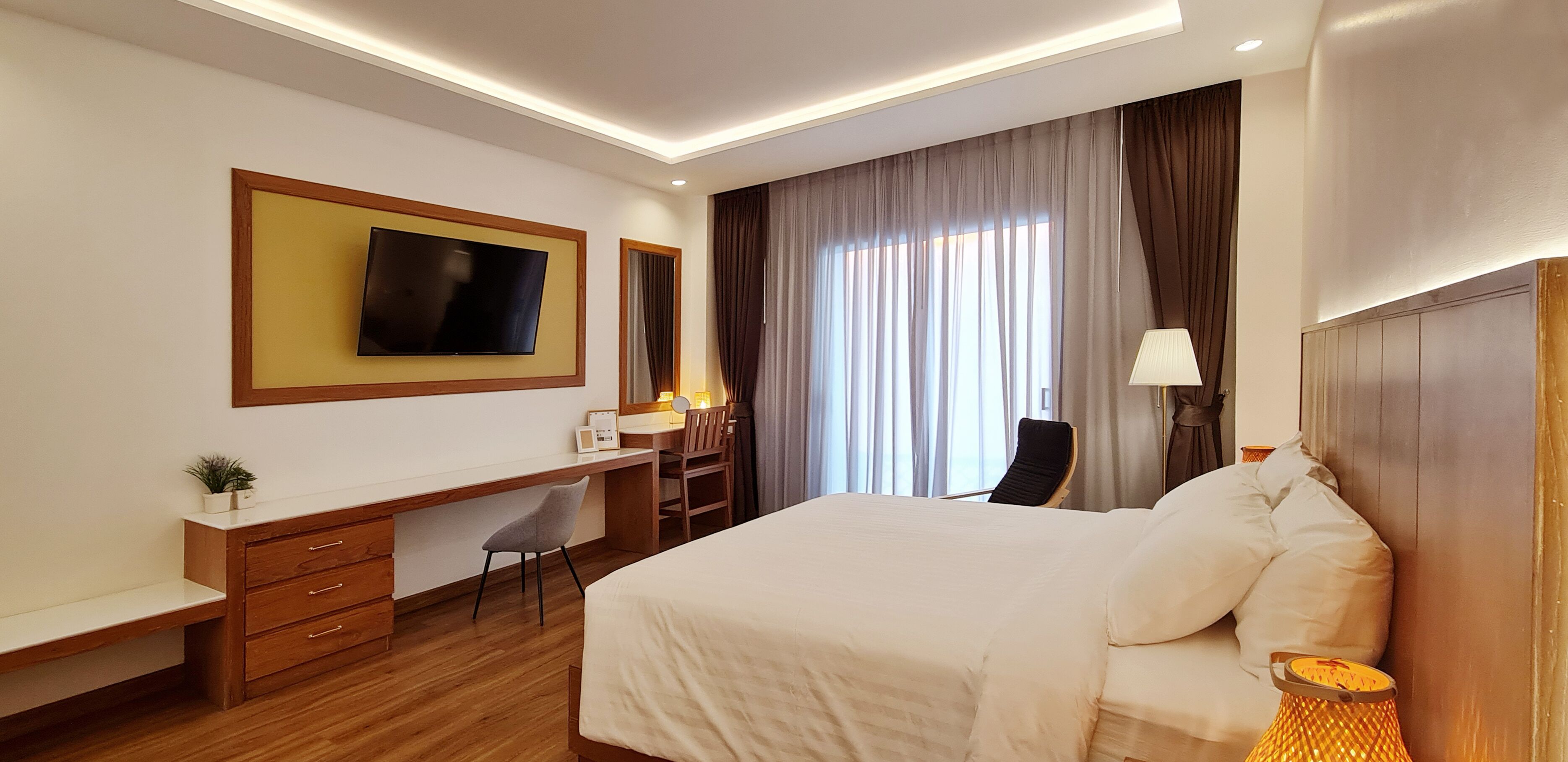 Una habitación de hotel con cama, escritorio, silla, televisor y lámpara.