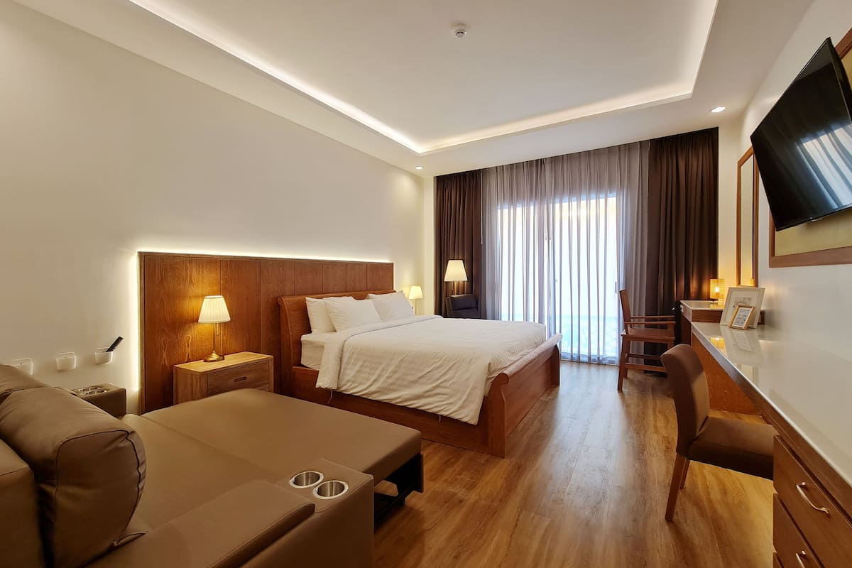 A hotel room with a bed, a desk, a chair, a TV, and a window with curtains.