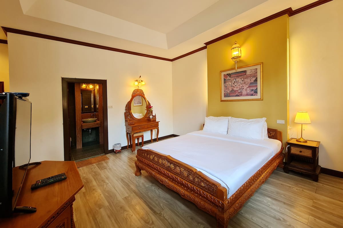 A hotel room with a large bed, a wooden dresser, a mirror, a bedside table with a lamp, and a television on a wooden stand.