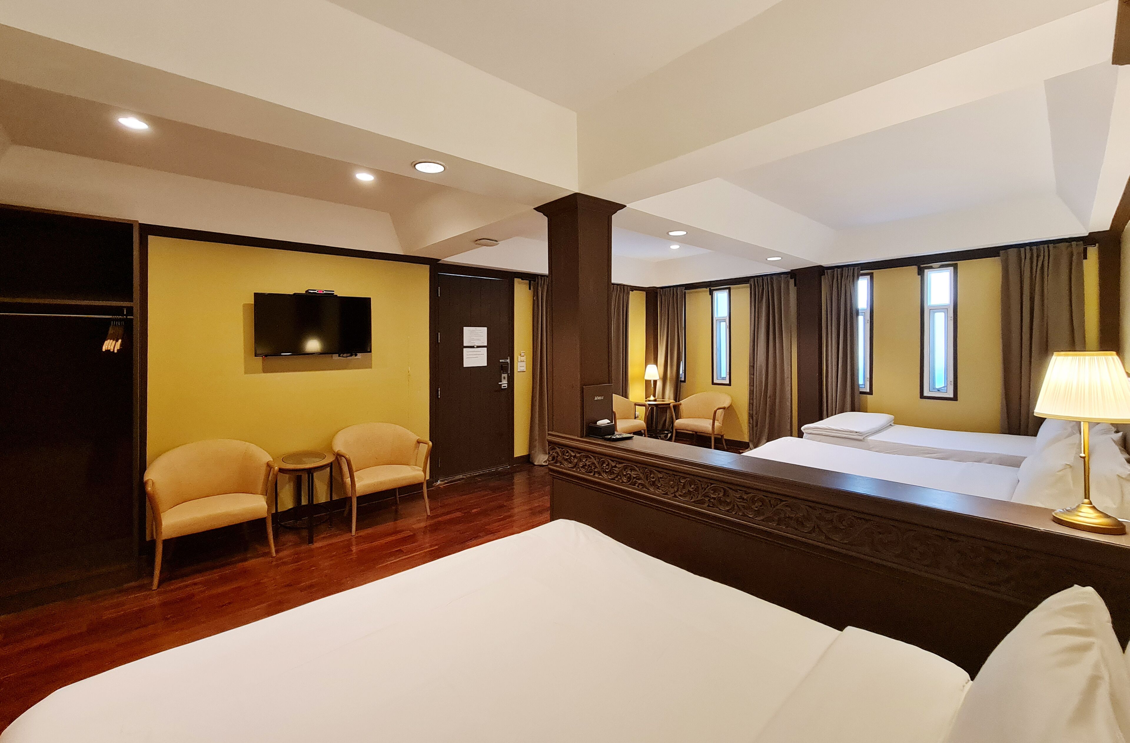 Une chambre d’hôtel avec un grand lit, deux fauteuils, une télévision et un bureau avec une lampe.