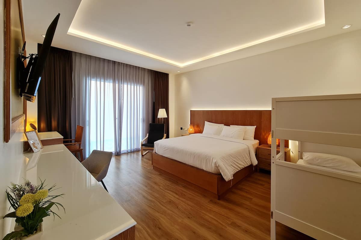 A modern hotel room with a large bed, a desk, a chair, a TV mounted on the wall, and a window with curtains.