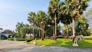 A well-maintained garden with palm trees, a statue, and a small building. - Phuphaphung Resort (Suan Phueng)