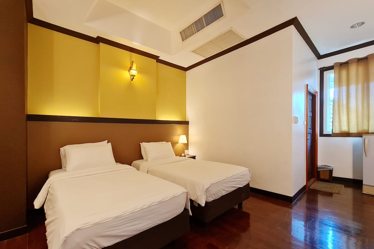 A hotel room with two beds, a wooden floor, and a window with curtains.