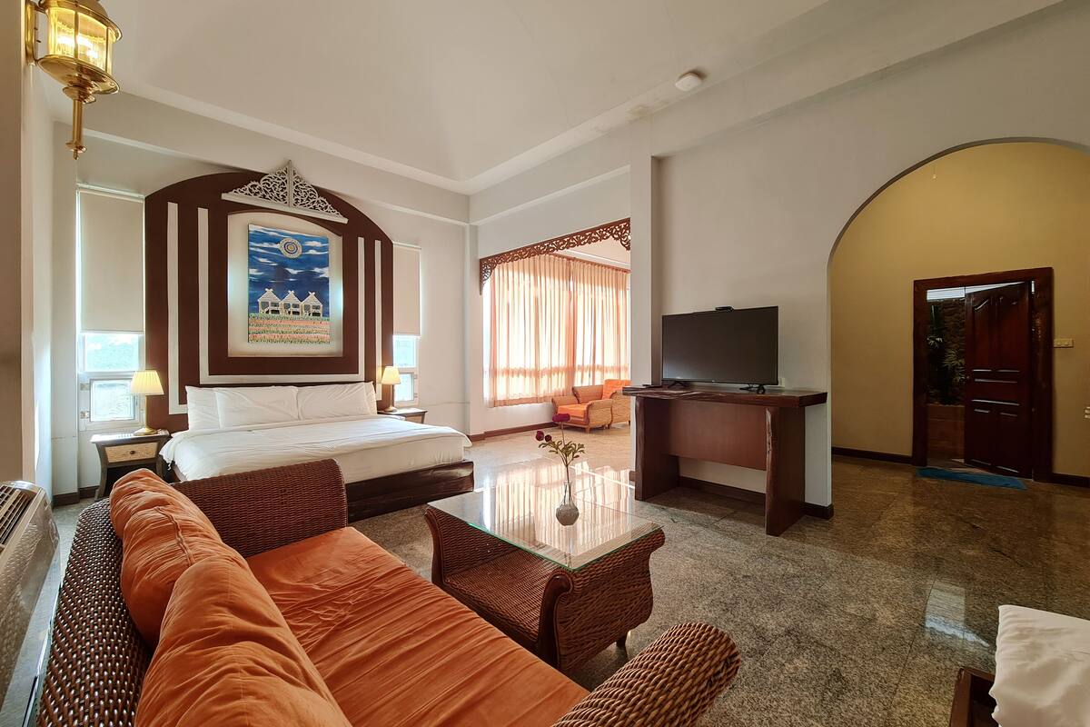 A hotel room with a bed, sofa, TV, and a decorative wall piece.