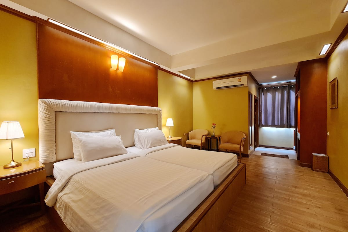 A hotel room with a large bed, two bedside tables with lamps, a chair, and an air conditioning unit.