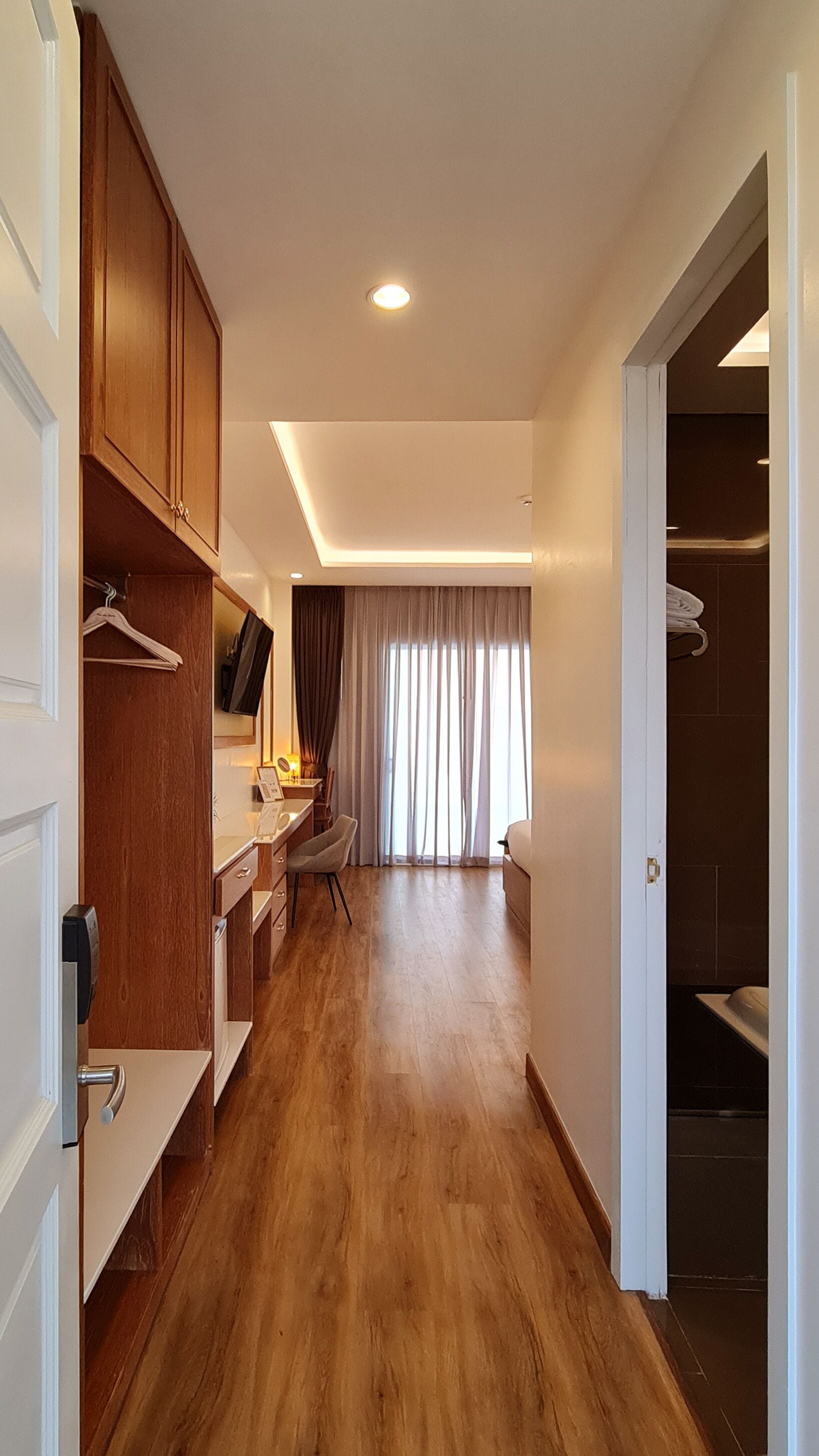Ein Hotelzimmer mit Holzboden, Schreibtisch mit Stuhl, Kleiderschrank und angrenzendem Badezimmer.